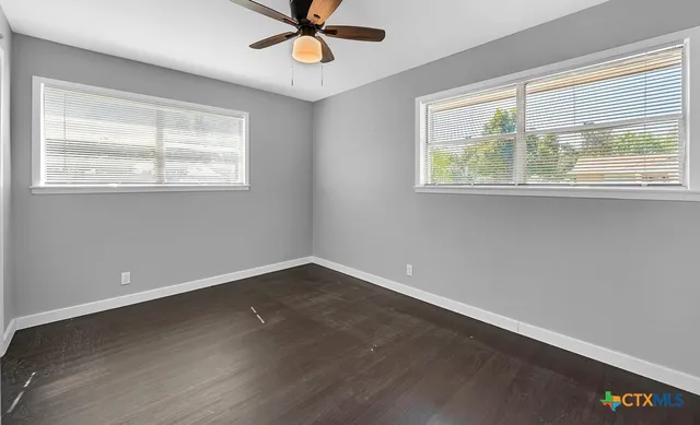 an empty room with wooden floor fan and windows
