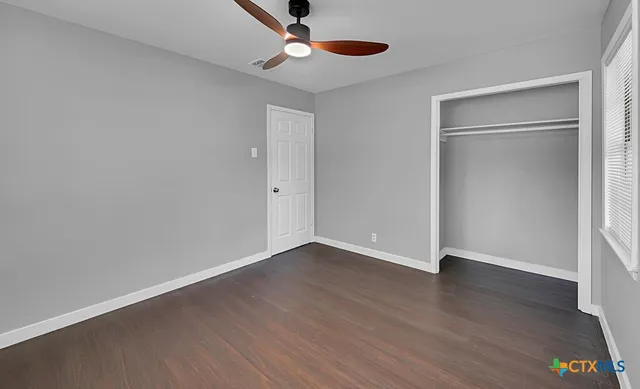an empty room with wooden floor a ceiling fan and windows