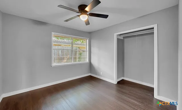 an empty room with wooden floor ceiling fan and windows