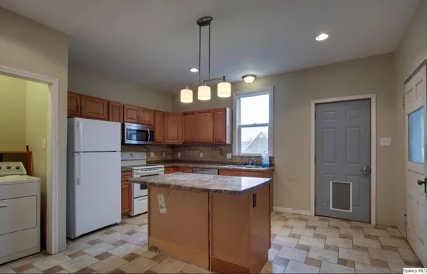 a kitchen with stainless steel appliances granite countertop a sink a refrigerator a stove a washer dryer and a dining table