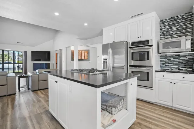 a kitchen with stainless steel appliances kitchen island granite countertop a stove a sink a refrigerator and white cabinets with wooden floor