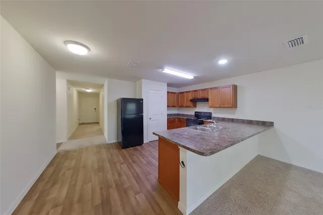 a kitchen with stainless steel appliances granite countertop a sink dishwasher a refrigerator and white cabinets with wooden floor