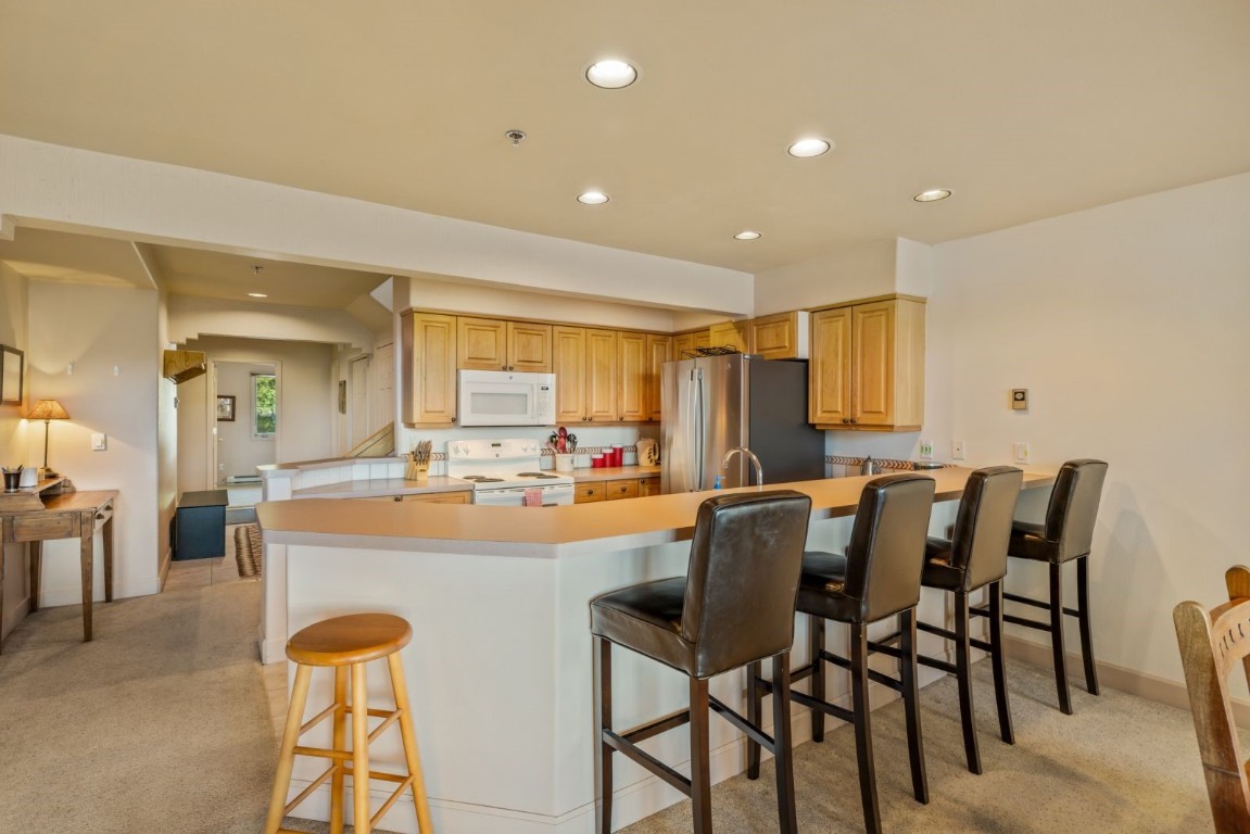 1724 Ski Time Square Drive, Unit R5 Steamboat Springs, CO 80487 - Photo 6 of 19 Kitchen featuring white appliances, a peninsula, recessed lighting, light carpet, and a breakfast bar area