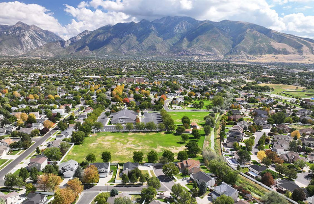 11675 South 300 East Draper, UT 84020 - Photo 2 of 5 Expansive residential area with a prominent mountain backdrop, featuring a large grassy field, paved streets, and numerous mature trees