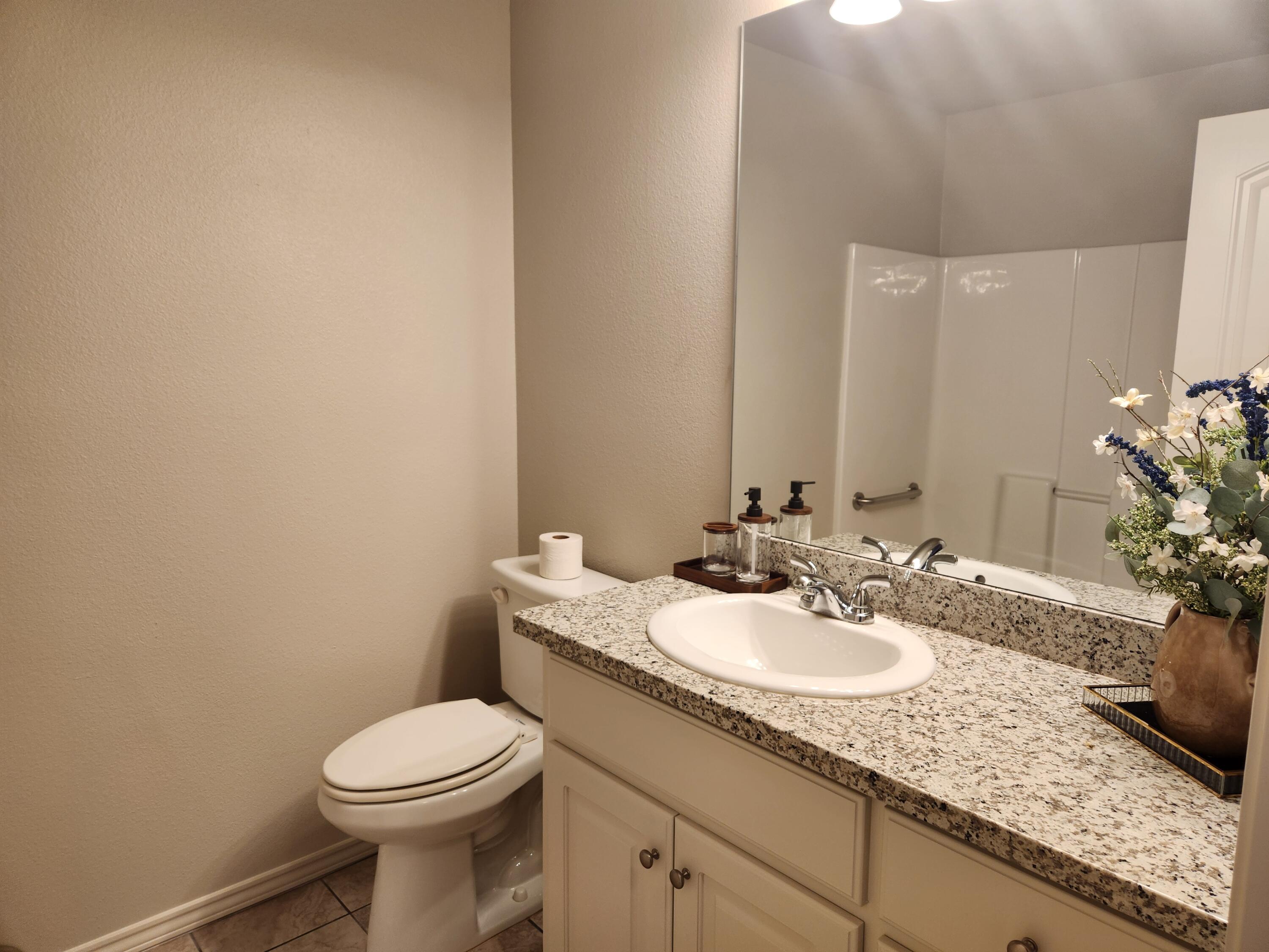 8702 13th Street Lubbock, TX 79416 - Photo 17 of 25 a bathroom with a granite countertop sink a toilet and mirror