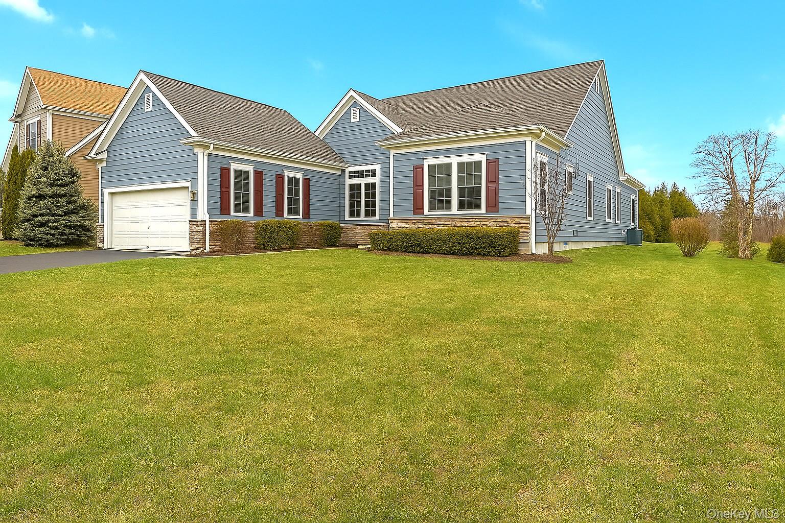 View of front facade featuring a garage, stone siding, a shingled roof, and driveway