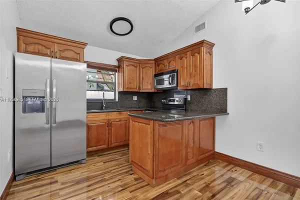 a kitchen with stainless steel appliances granite countertop a refrigerator a stove and a sink with wooden floor