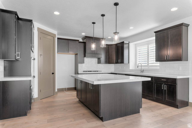 2724 Mt Jordan Road Sandy, UT 84092 - Photo 14 of 33 Kitchen with pendant lighting, light wood-type flooring, dark wood finish cabinets, a kitchen island, and light stone counters