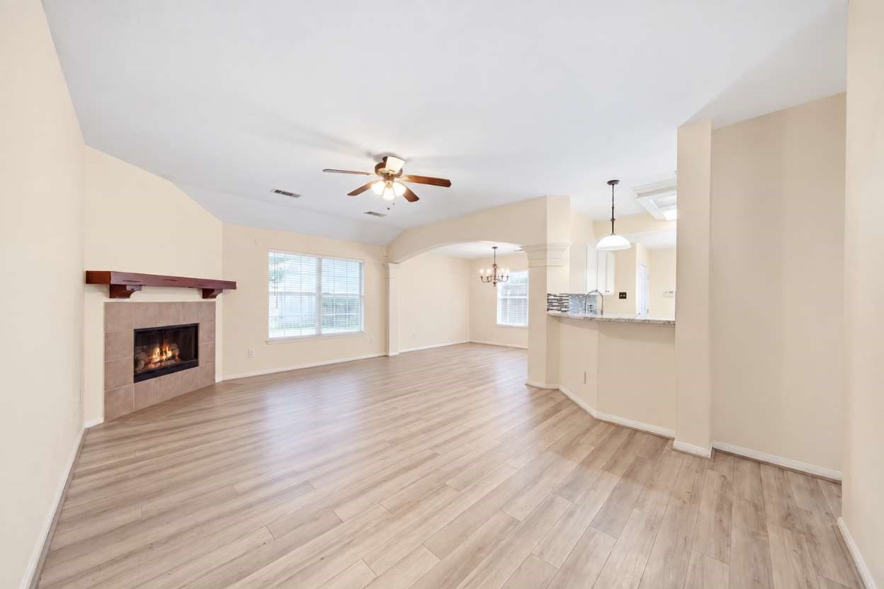 6911 River Road Richmond, TX 77469 - Photo 9 of 36 High vaulted ceilings and low-maintenance wood-look flooring enhance the open layout of this central living area, highlighted by a corner gas-log fireplace with a classic mantle. Arched architectural openings connect effortlessly to the formal dining space and kitchen breakfast bar, maximizing functional entertainment space.