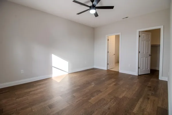 an empty room with wooden floor fan and windows