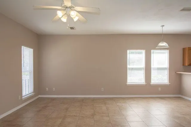 an empty room with chandelier fan and windows