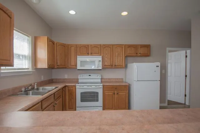 a kitchen with granite countertop a refrigerator sink stove and white cabinets