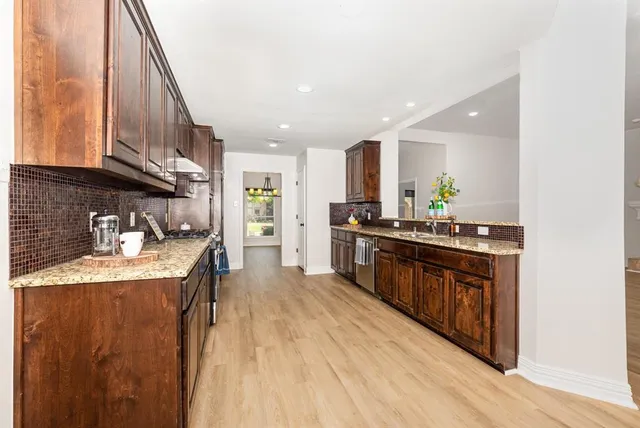 a kitchen with stainless steel appliances granite countertop a stove a sink dishwasher and a refrigerator with wooden floor