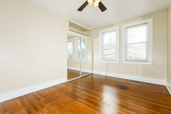 an empty room with wooden floor fan and windows