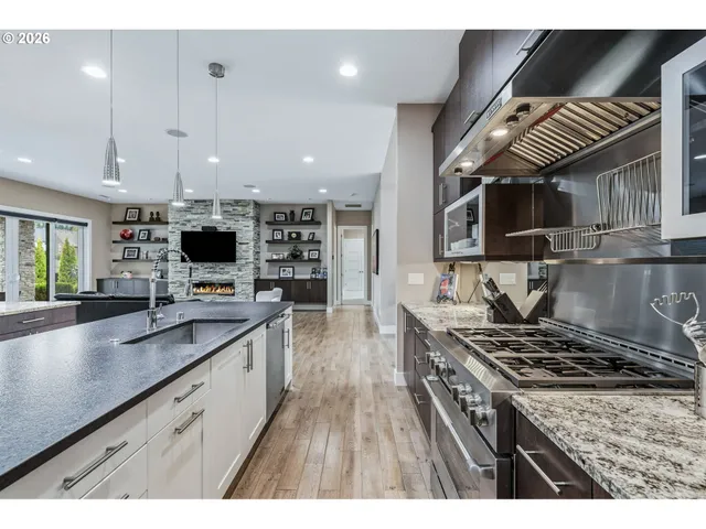 a kitchen with stainless steel appliances kitchen island granite countertop a stove top oven a sink dishwasher and white cabinets with wooden floor