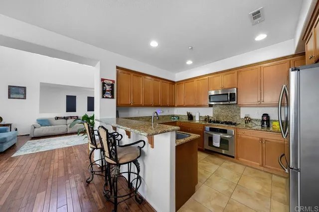 a kitchen with stainless steel appliances granite countertop a stove top oven a sink dishwasher a dining table and chairs with wooden floor