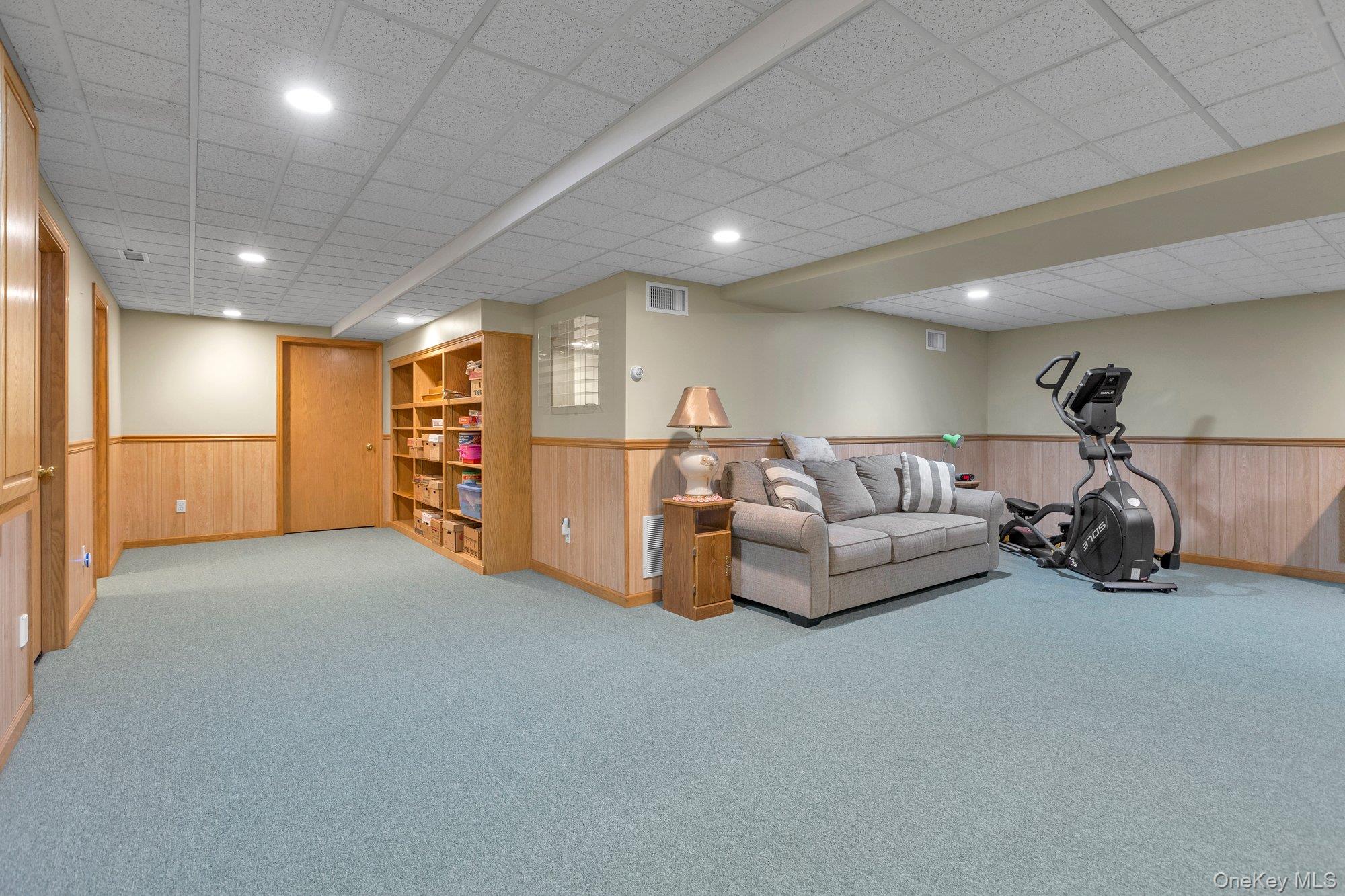 501 Wading River Road Manorville, NY 11949 - Photo 25 of 31 Living area with carpet, recessed lighting, a drop ceiling, and wood walls