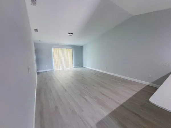 a view of an empty room with wooden floor and window