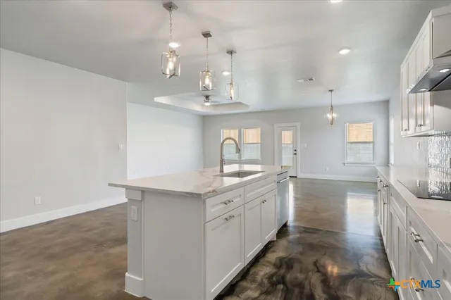 a large kitchen with stainless steel appliances a large counter top a sink and a chandelier
