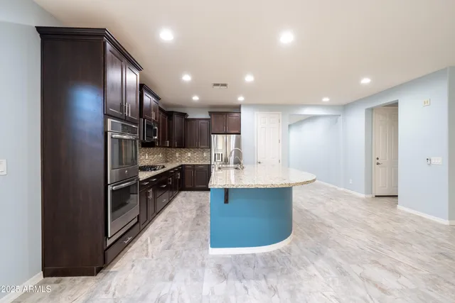 a large kitchen with stainless steel appliances kitchen island a large counter top and wooden floors