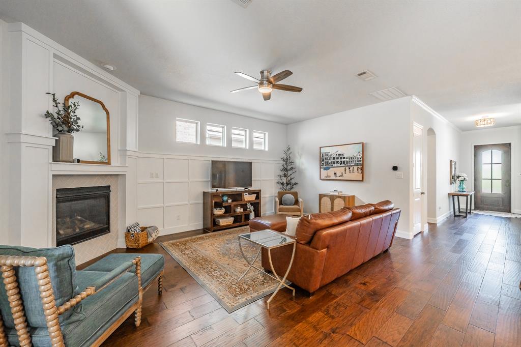 1205 Ivy Charm Way Arlington, TX 76005 - Photo 17 of 40 Dark wood-finish flooring extending into the entry, a corner fireplace with white surround, decorative wall paneling, and a ceiling fan with integrated lighting