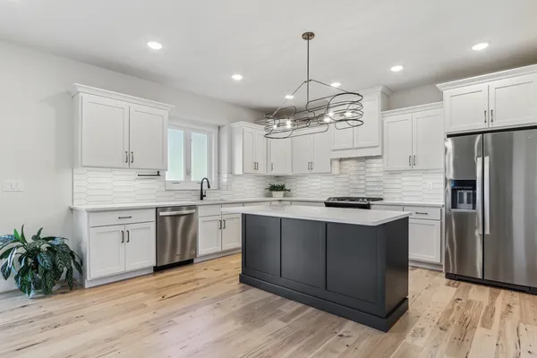 a open kitchen with stainless steel appliances granite countertop a stove a sink dishwasher a refrigerator and a dining table with wooden floor