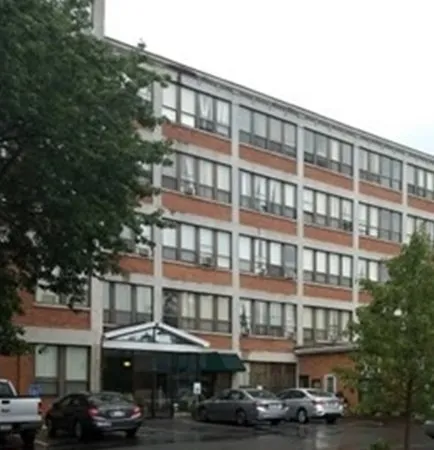 a front view of a building with lot of cars and trees