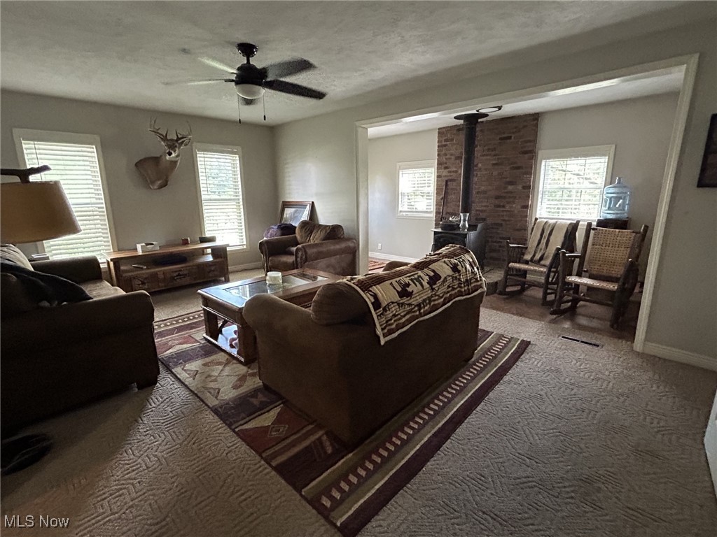 4853 Leon Road Andover, OH 44003 - Photo 6 of 33 Carpeted living room with a textured ceiling, brick wall, ceiling fan, and a wood stove