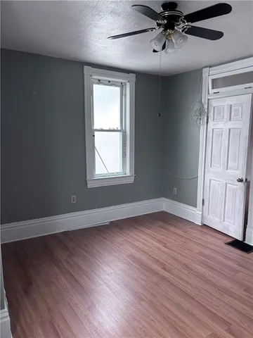 an empty room with wooden floor chandelier fan and windows