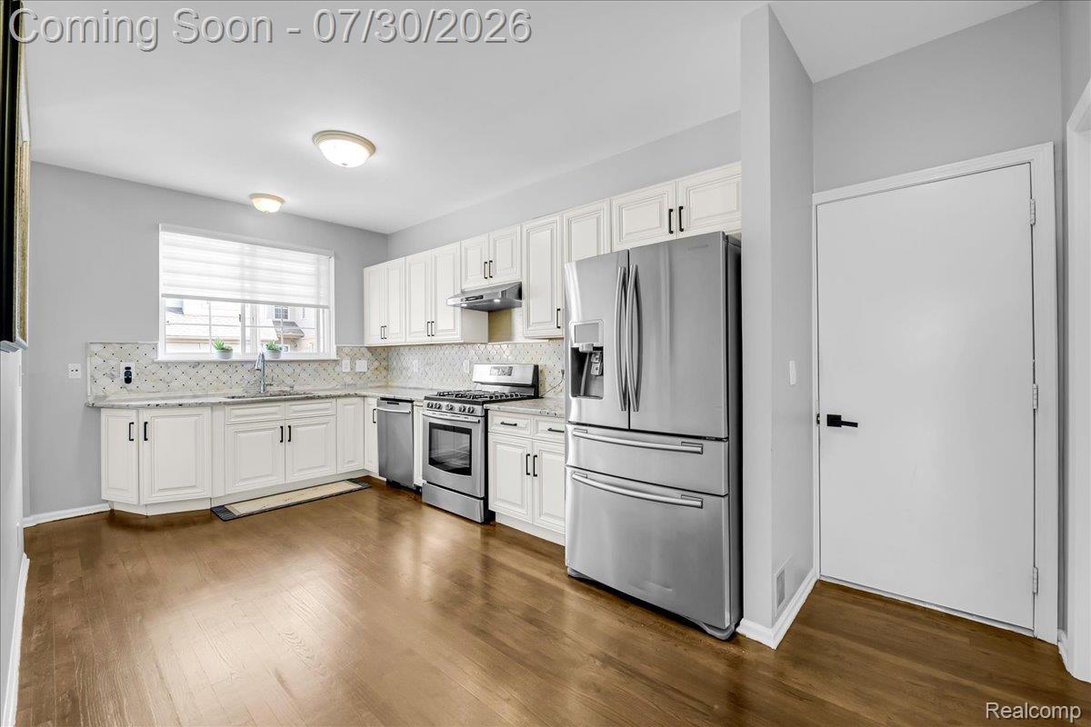 41447 Glade Road Canton, MI 48187 - Photo 11 of 28 Kitchen featuring wood-finish flooring, white cabinetry with black hardware, stainless steel appliances, granite countertops, and a subway tile backsplash