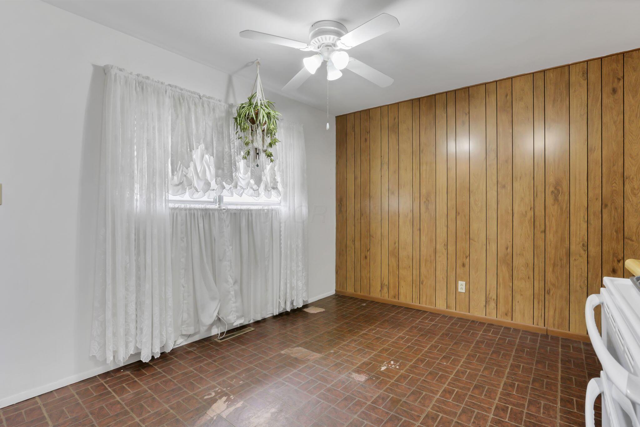 3882 Glenfield Road Columbus, OH 43232 - Photo 13 of 29 Eat-in space featuring white painted walls, wood-paneled accent wall, a window with white sheer curtains, and a ceiling fan with light fixture