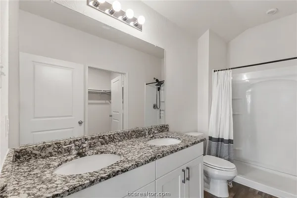 a bathroom with a granite countertop sink a toilet a mirror and shower