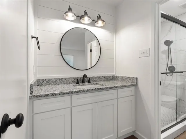 a bathroom with a granite countertop sink a mirror and shower