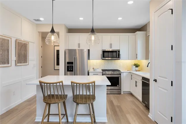 a kitchen with stainless steel appliances a dining table chairs stove refrigerator and microwave