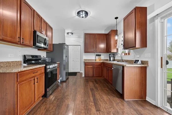 a kitchen with stainless steel appliances granite countertop wooden cabinets a refrigerator a sink a stove a microwave and wooden floors