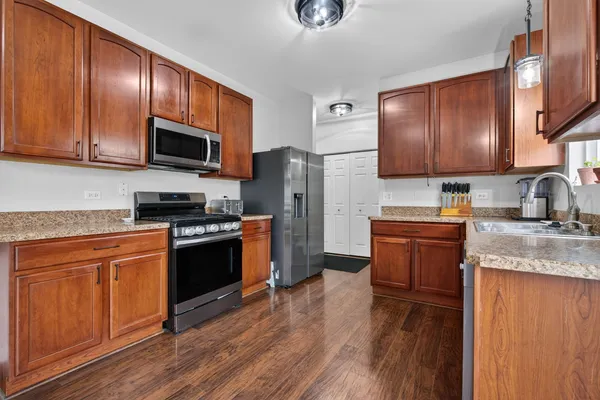 a kitchen with granite countertop wooden cabinets a stove a oven and a refrigerator with wooden floor
