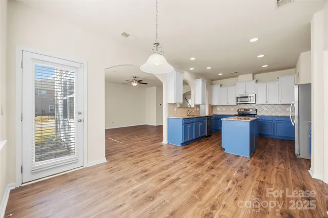 a kitchen with stainless steel appliances kitchen island granite countertop wooden floors wooden cabinets and entryway