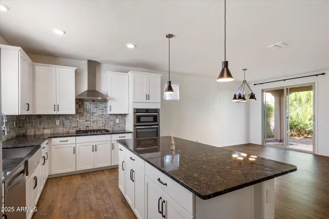 a kitchen with stainless steel appliances granite countertop a sink a stove a refrigerator and white cabinets with wooden floor