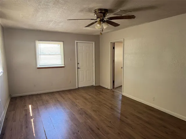 a view of an empty room with wooden floor and a ceiling fan