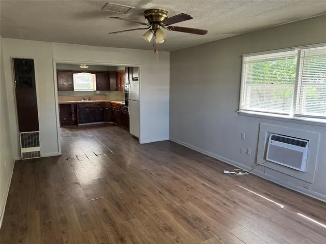 a view of a kitchen and an empty room with wooden floor and a window