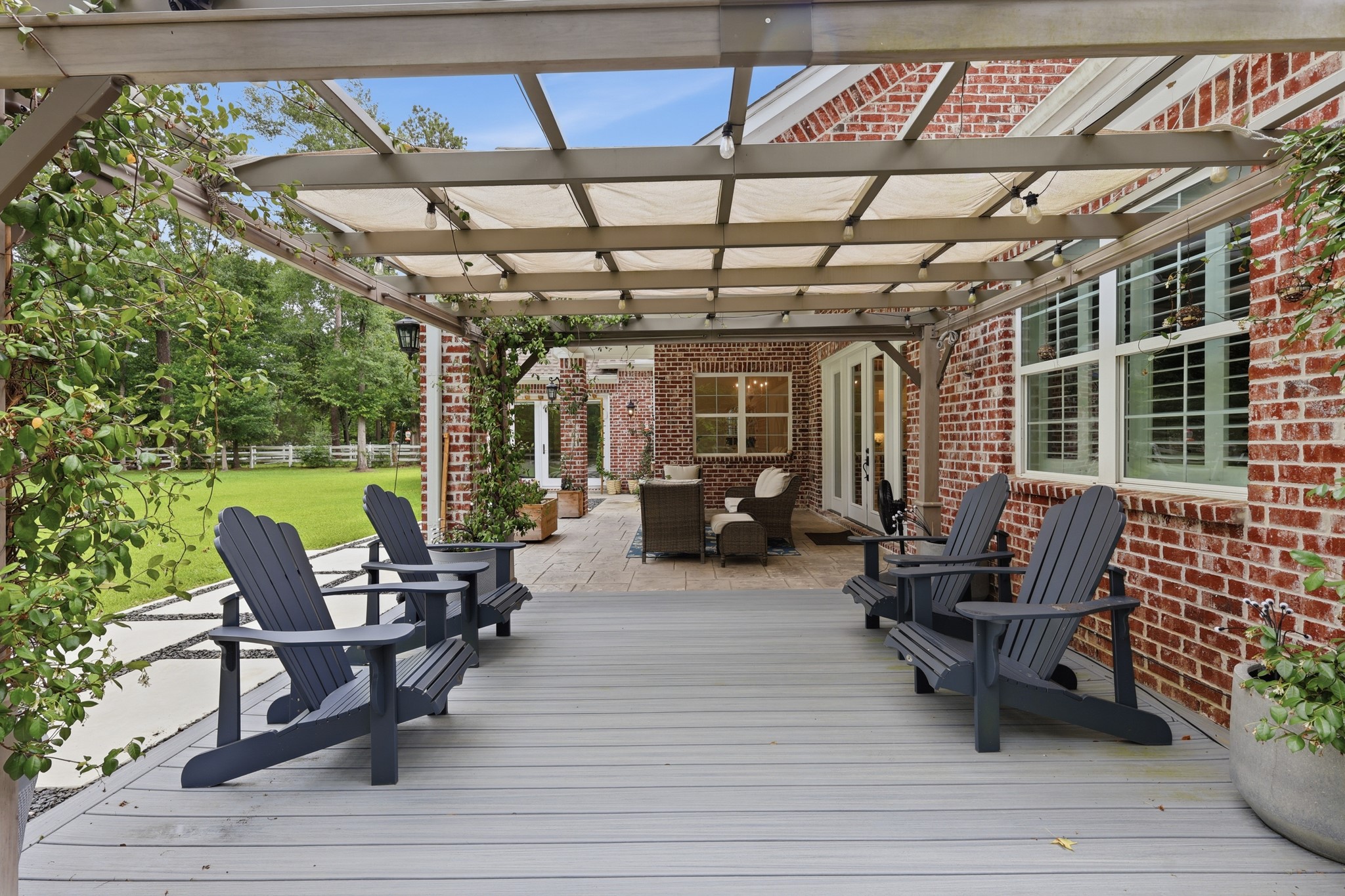 7106 Hampton Court Spring, TX 77389 - Photo 24 of 31 Outdoor space features a spacious deck with a pergola, perfect for relaxation. It includes Adirondack chairs, lush greenery, and a view of a well-maintained lawn, all set against a charming brick exterior.