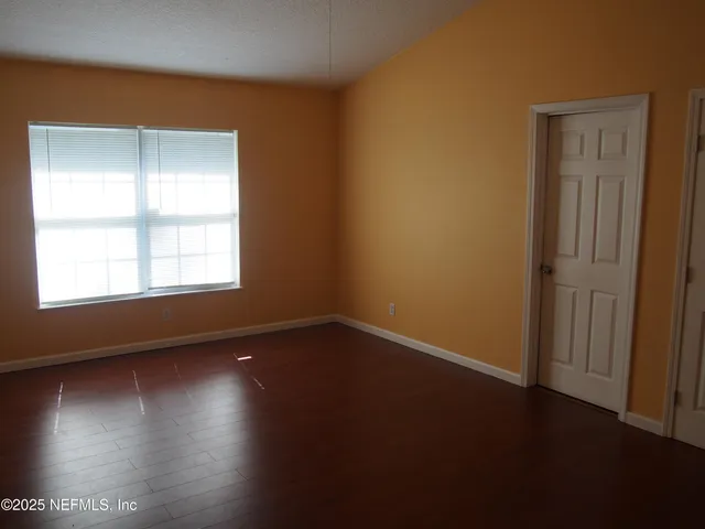 an empty room with wooden floor and windows with curtains