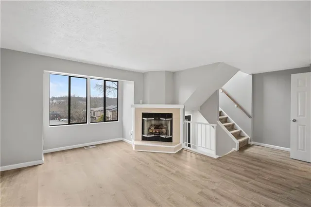 a view of an empty room with wooden floor fireplace and a window