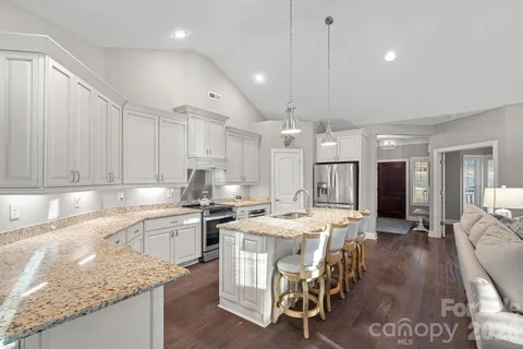 a kitchen with stainless steel appliances granite countertop a stove top oven a sink a refrigerator and white cabinets
