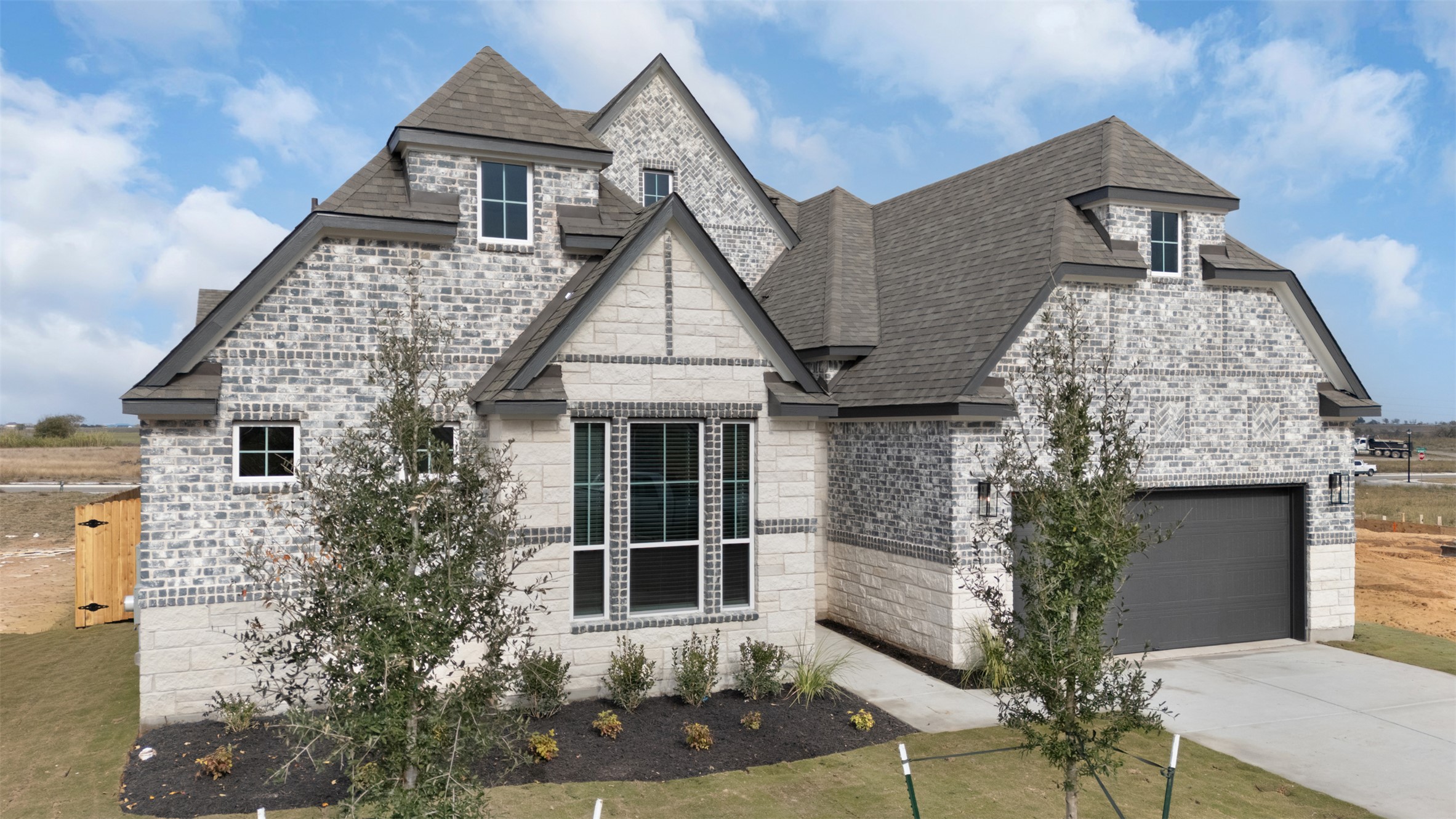 2312 Tobiano Trace Georgetown, TX 78633 - Photo 2 of 33 Multi-gabled roofline with dormer windows, featuring a mixed stone and brick facade, an attached garage with a dark panel door, and manicured landscaping