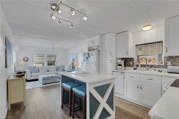 a kitchen with stainless steel appliances granite countertop a stove a refrigerator a kitchen island white cabinets and couches with wooden floor