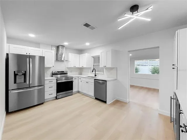 a large kitchen with stainless steel appliances kitchen island a large counter top and wooden floors