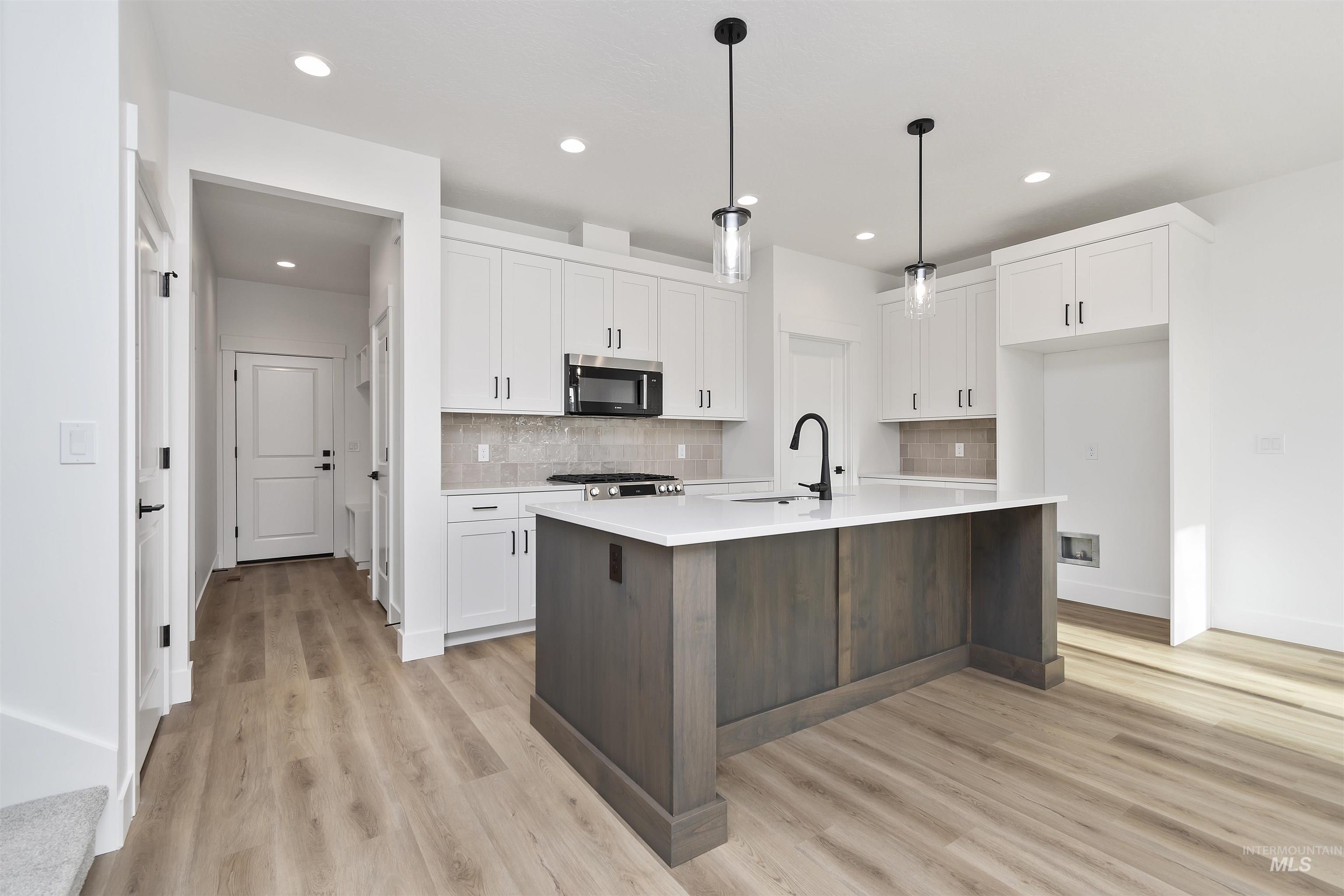 764 South Calhoun Lane Star, ID 83669 - Photo 9 of 48 Kitchen featuring white cabinetry, a center island with sink, dark brown cabinets, hanging light fixtures, and stainless steel appliances