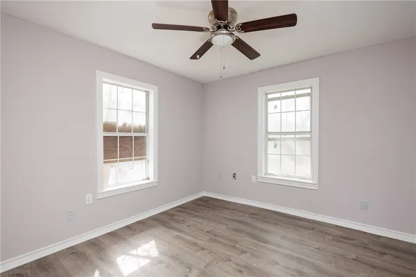 an empty room with wooden floor fan and windows