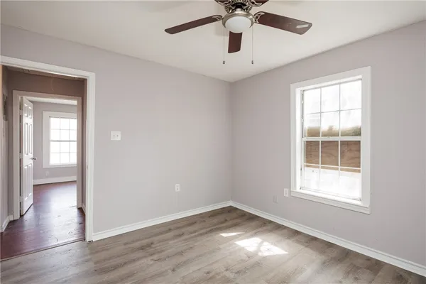 an empty room with wooden floor chandelier fan and windows